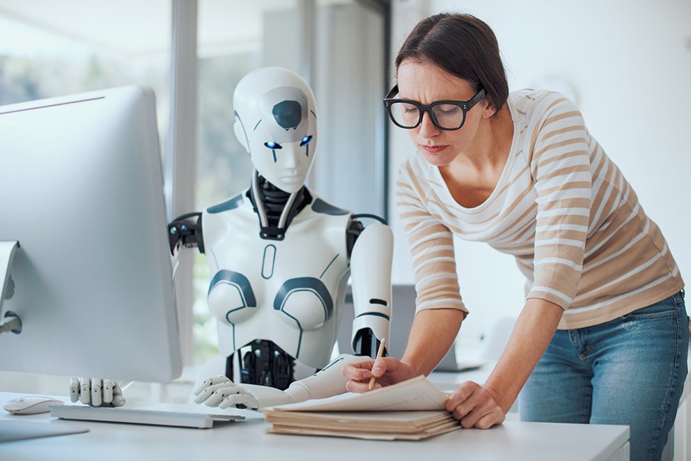 Ein humanoider Roboter und eine Frau befinden sich zusammen hinter einem Schreibtisch, als bildlichen Hinweis auf KI Recruiting