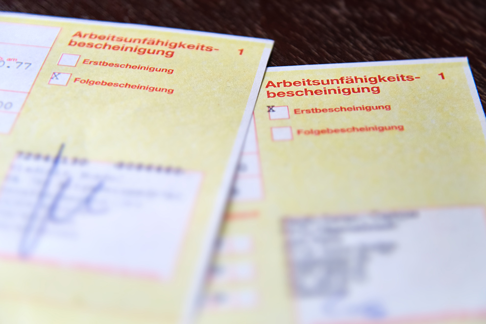 Zwei gelbe Arbeitsunfähigkeitsbescheinigungen liegen auf einem Tisch – Symbolbild für Krankheitstage