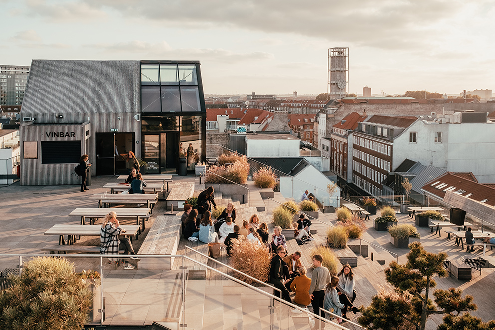Menschen sitzen auf Stufen an einer Rooftopbar, die die Stadt Aarhus überblickt