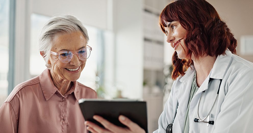 Eine Ärztin erklärt ihrer Patientin etwas, während sie ein Tablet in der Hand hält, als Symbol für das Thema KI im Gesundheitswesen