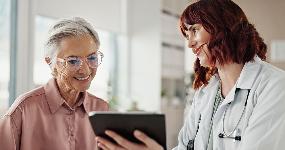 Eine Ärztin erklärt ihrer Patientin etwas, während sie ein Tablet in der Hand hält, als Symbol für das Thema KI im Gesundheitswesen