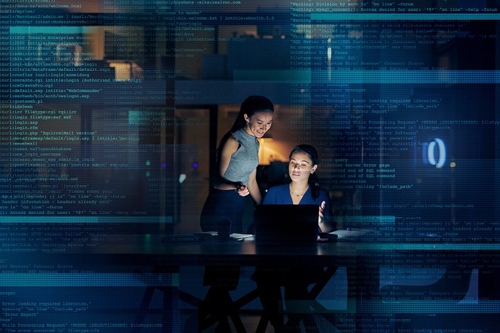 Zwei junge Frauen, die sich hinter einem Schreibtisch mit Laptop über das Thema Generative Engine Optimization unterhalten